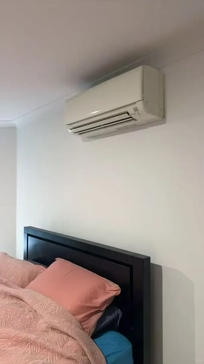 Wall-mounted indoor air conditioning unit above a bedroom wall